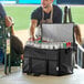 A man in an apron holding a Choice black large insulated cooler bag full of cans of soda.