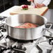 A chef braising meat in a Vollrath Intrigue brazier on a stove.