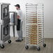 A man standing next to an Advance Tabco bun and sheet pan rack filled with trays.