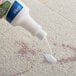 A hand uses Noble Chemical Spot-B-Gone to pour liquid onto carpet.
