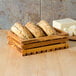 An American Metalcraft Olive Wood Bread Crate on a counter with bread and cheese inside.