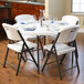 A white Lifetime round folding table with white chairs, plates, and silverware on it.