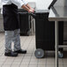 A chef pushing a black Carlisle mobile ice bin with wheels.