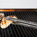 Vollrath Jacob's Pride VersaGrip tongs with tan coated Kool Touch handles cooking on a grill.