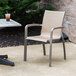 A Grosfillex Sunset Cognac outdoor stacking armchair on a patio.