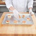 A person in white gloves putting cinnamon rolls on a Chicago Metallic aluminum sheet pan.