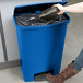 A woman using a Rubbermaid blue plastic Slim Jim trash can to throw away garbage.