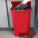 A woman using a black case to put a bag in a red Rubbermaid Slim Jim trash can.