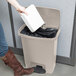 A woman using a Rubbermaid Slim Jim front step-on trash can to put a white box inside.