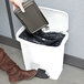 A woman's hand using a Rubbermaid Slim Jim white front step-on trash can to put a black plastic bag into a trash can.