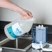 A hand pouring Noble Chemical Novo Alcohol-Free Foaming Hand Sanitizer into a dispenser.