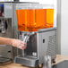 A person pouring orange liquid into a Crathco beverage dispenser.