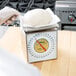 A person wearing white gloves weighing a white ball of dough on an Edlund portion scale.