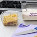 A clear plastic Cambro food storage container with pasta and a knife on a counter.