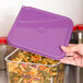 A person's hand holding a purple Cambro lid over a container of pasta.