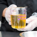 A person in a white coat using a Cambro purple polycarbonate measuring cup to pour yellow liquid.