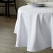 A table with a white Intedge polyester tablecloth and white plates on it.