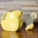 A yellow Fiesta disc pitcher filled with water and lemons on a wood surface.