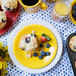 A yellow Fiesta® appetizer plate with a blueberry muffin on it on a table with other food items.