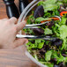 A person using Fineline silver plastic tongs to serve salad