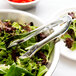 A bowl of salad with silver tongs.