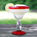 A Libbey Aruba margarita glass with a drink on it, with a red rim and base, filled with a margarita and garnished with a lime.