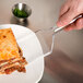 A hand holding a Fineline clear disposable spatula over a lasagna.
