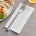 A fork and knife on a white plate with a Touchstone by Choice white linen-feel dinner napkin.