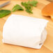 A white paper bag on a table with a sandwich wrapped in white paper.