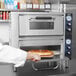 A person putting a pizza into a Waring countertop pizza oven.