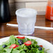 A clear plastic Dinex lid with a straw slot on a plastic cup of water next to a plate of salad.