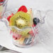 A clear plastic Cambro swirl bowl filled with fruit.