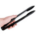 A person holding a pair of black Fineline disposable plastic tongs.