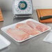 A white CKF foam meat tray with raw chicken on a counter.
