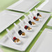 A group of Elite Global Solutions white rectangular melamine serving platters with spoons filled with fruit and yogurt.