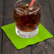 A glass of ice and a Creative Converting Fresh Lime Green beverage napkin with a straw.