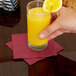 A hand holding a glass of orange juice with a burgundy beverage napkin on the table
