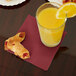 A glass of orange juice next to a plate of pastries with a burgundy Creative Converting beverage napkin.