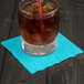 A glass with ice and a straw on a Bermuda Blue Creative Converting beverage napkin.