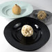 A group of Elite Global Solutions black round bowls with fruit on them.
