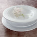 A stack of white Elite Global Solutions Durango melamine plates with a white flower on top.