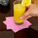 A person holding a glass of orange juice on a pink Creative Converting beverage napkin.