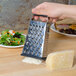 A hand grates cheese with a Tablecraft stainless steel box grater.
