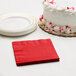 A white cake with red sprinkles next to a red Creative Converting Classic Red beverage napkin.