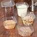 Square plastic deli containers with white lids holding nuts, chocolate, and other food.