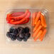A clear plastic deli container with three compartments holding a variety of fruits and vegetables, including carrots and a red pepper.