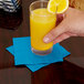 A hand holding a glass of orange juice with a turquoise blue Creative Converting beverage napkin inside.