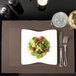 A plate of salad, a glass of wine, and a Snap Drape Reno chocolate placemat on a table.