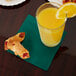 A table with a glass of orange juice and a Creative Converting hunter green beverage napkin holding pastries.