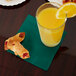 A table with a glass of orange juice and a Creative Converting hunter green beverage napkin holding pastries.